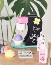 Load image into Gallery viewer, Black and pink wooden toy shave ice machine with toy syrup bottles, menu, and purple, pink, and orange shave ice pieces.