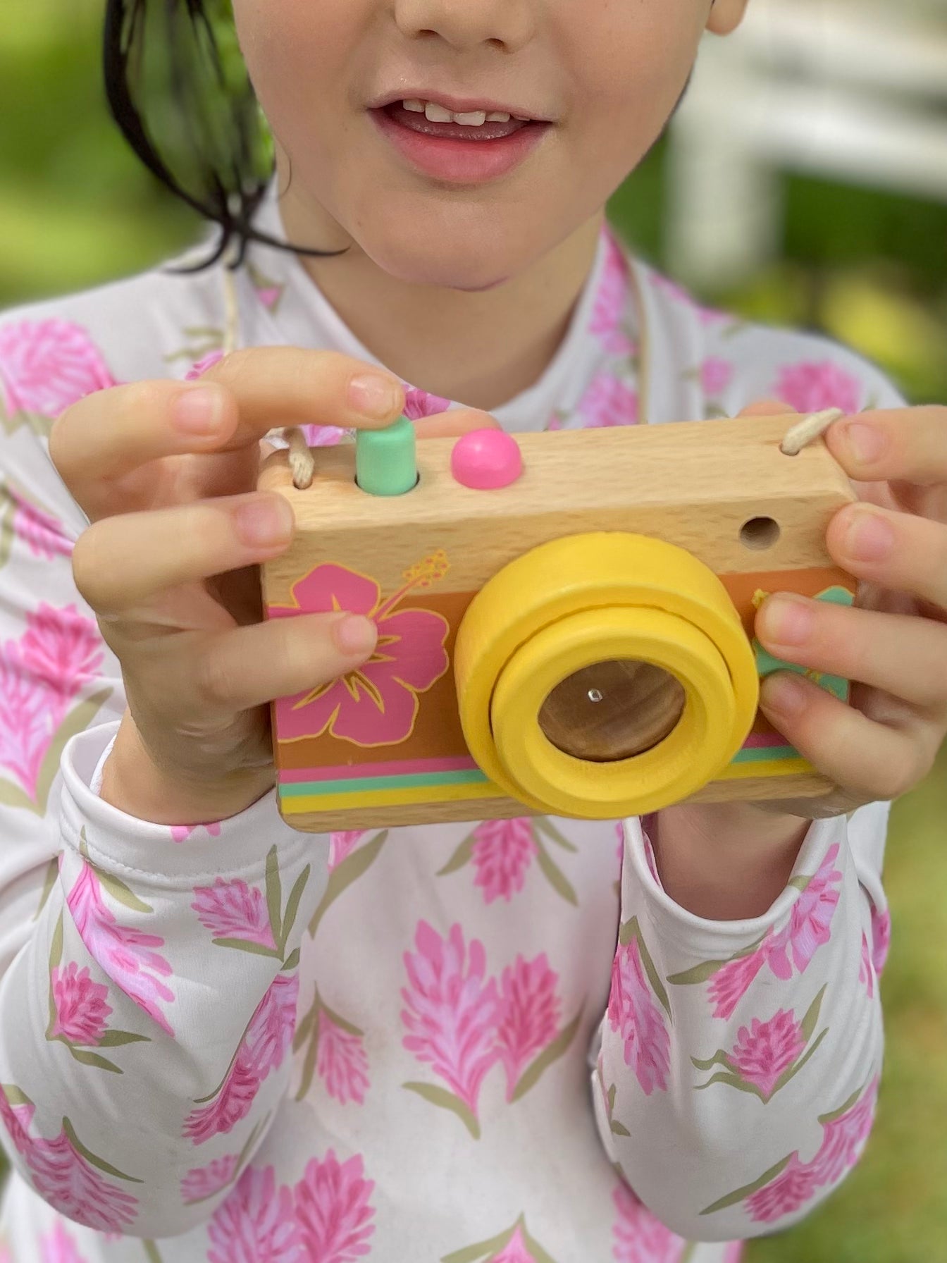 Little girl pushing the teal button on the wooden camera