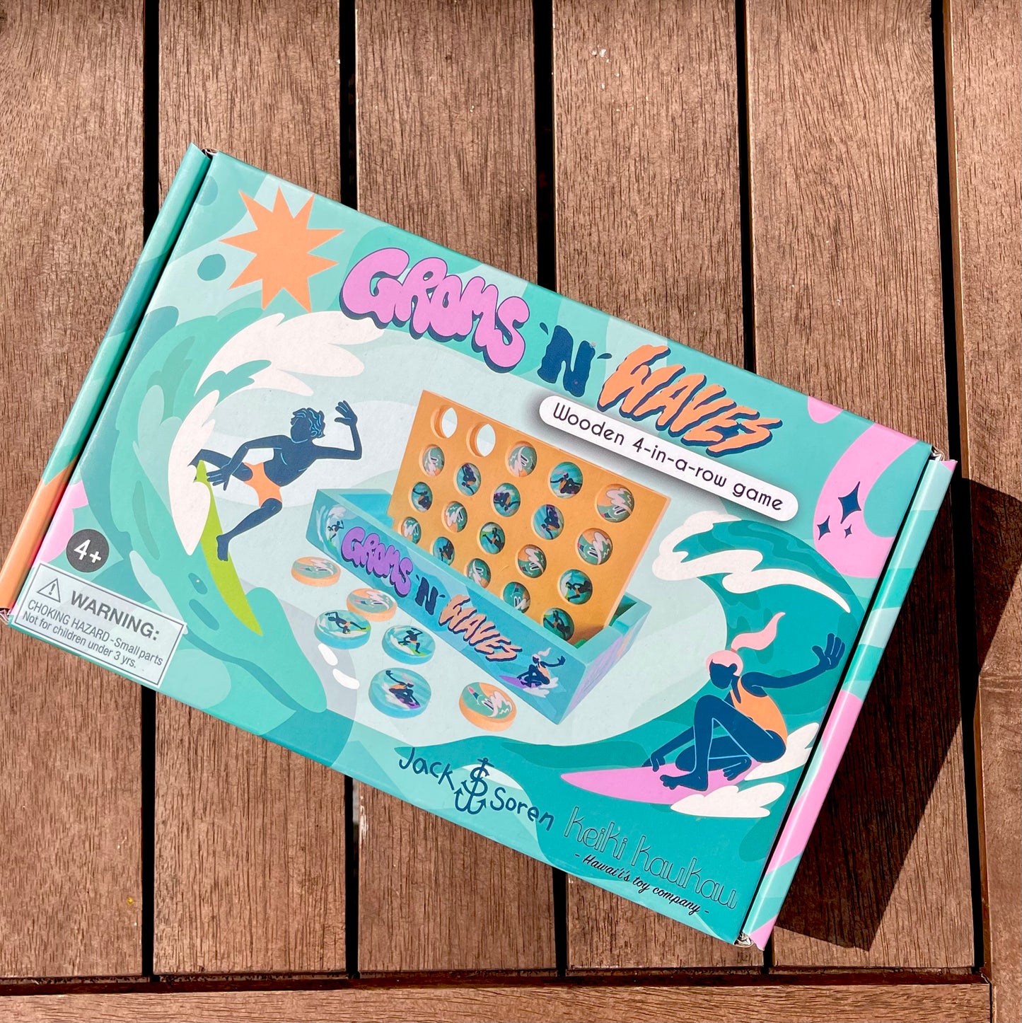 Teal box with surfers on it reading "Groms 'n' Waves" 