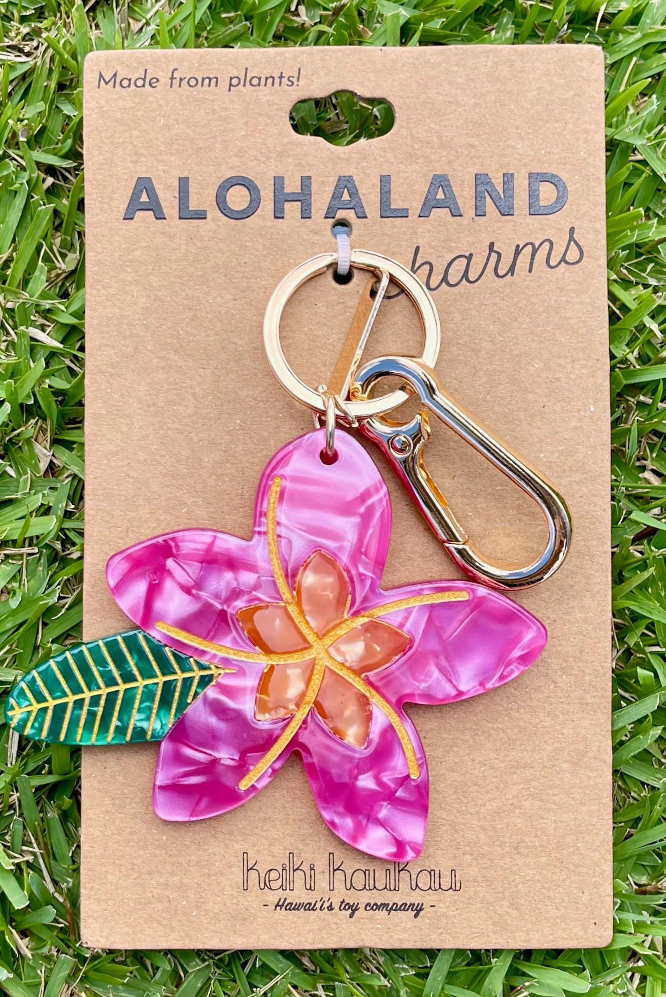 Keychain with pink flower design on a 'Alohaland' branded card against a grass background