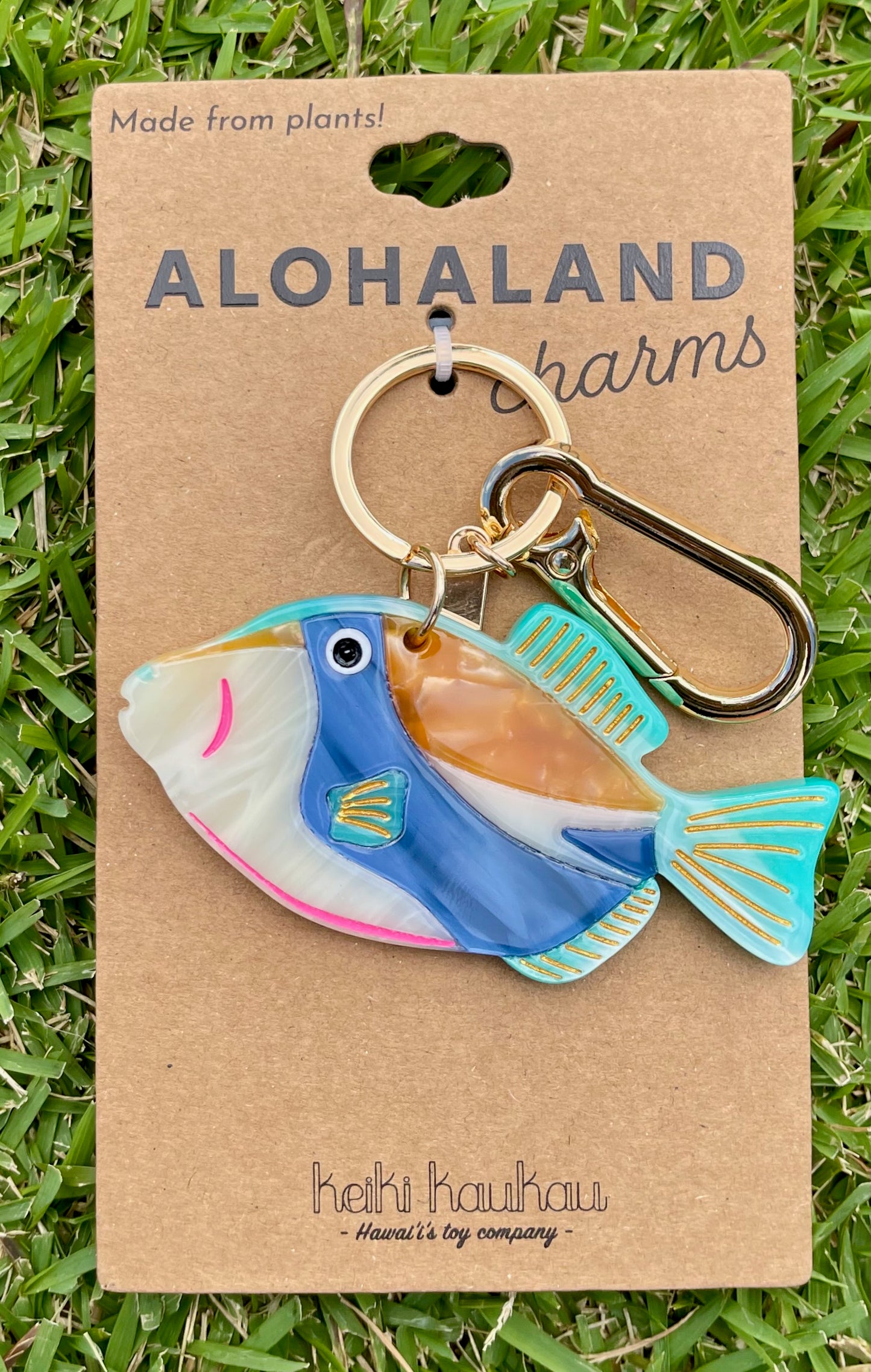 Humuhumunukunukuapua‘a fish-shaped keychain on a 'Alohaland Charms' card with grass background