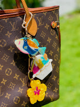 Load image into Gallery viewer, Colorful fish keychain attached to a brown patterned handbag with a blurred green background
