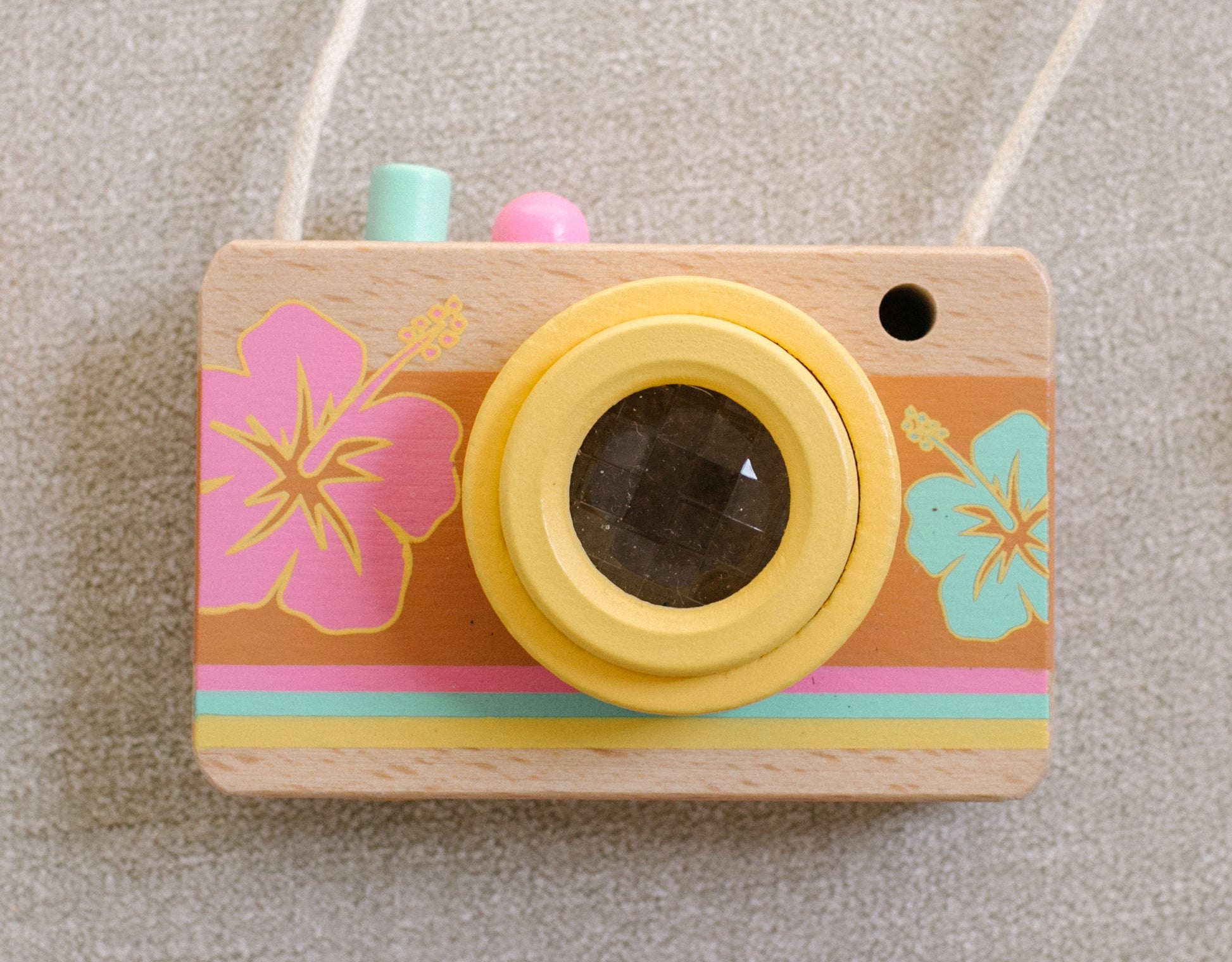 Wooden camera with a kaleidoscopic lens painted with a pink and a teal hibiscus flower.