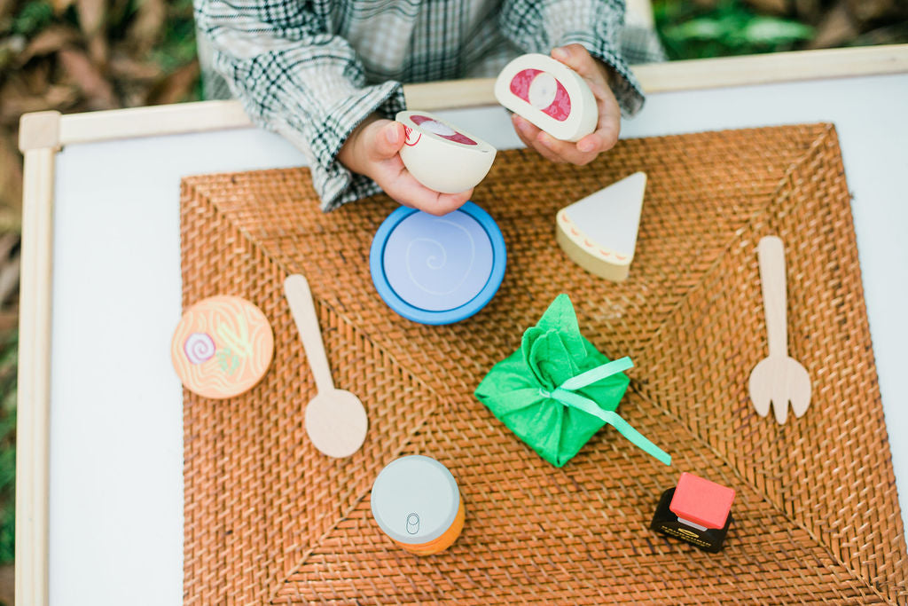Child playing with more keiki kaukau wooden play food set at a table