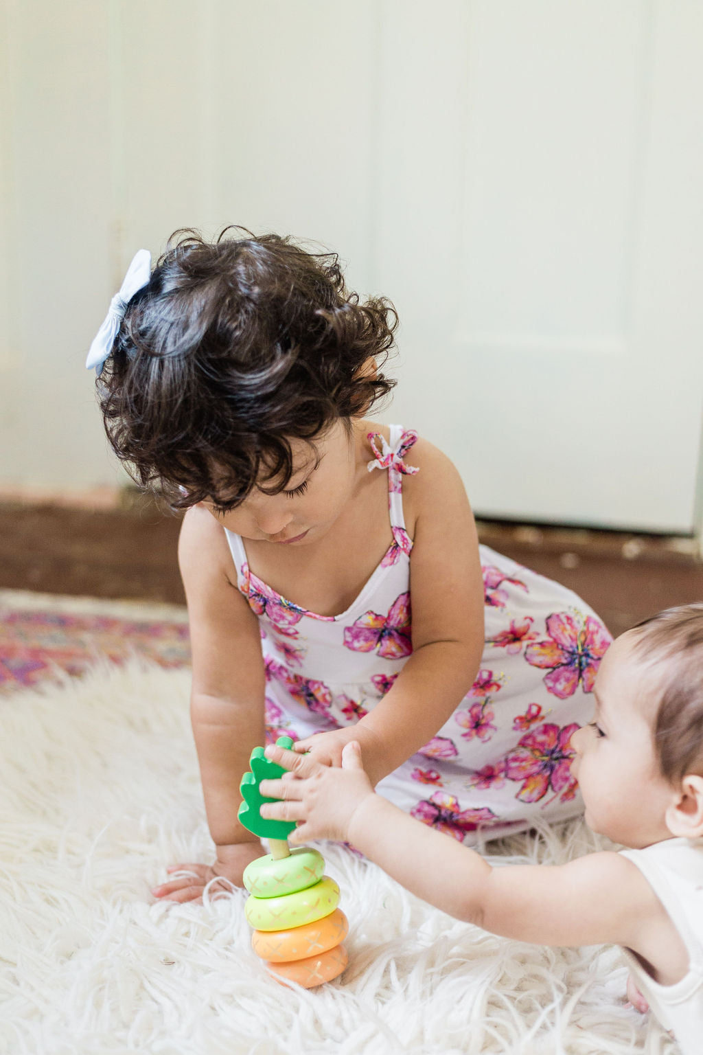little girl and baby playing with a yellow wooden pineapple stacking toy 