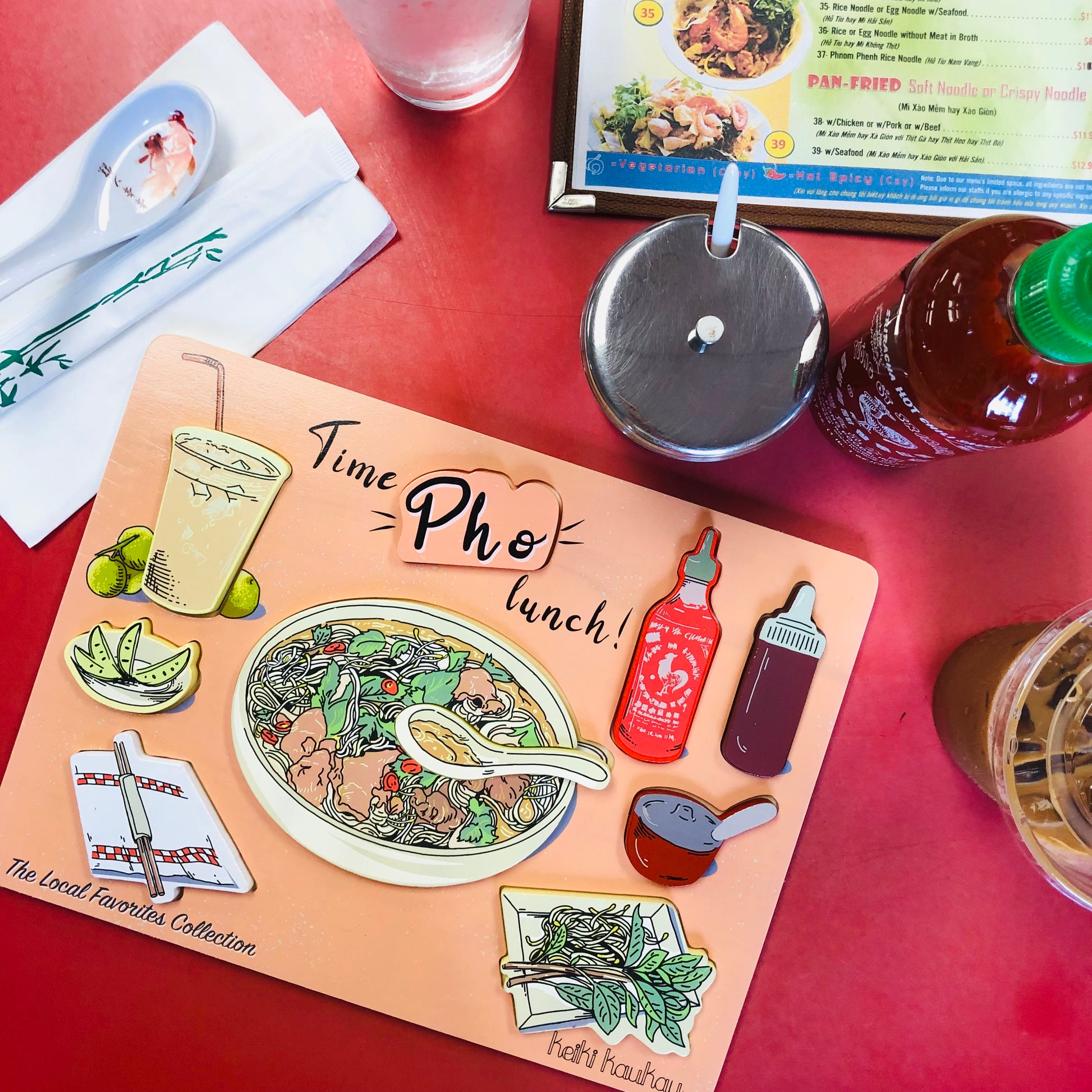 Completed pastel orange Vietnamese food puzzle next to bottle of siracha, Vietnamese food menu, and soup spoon and chopsticks on a napkin