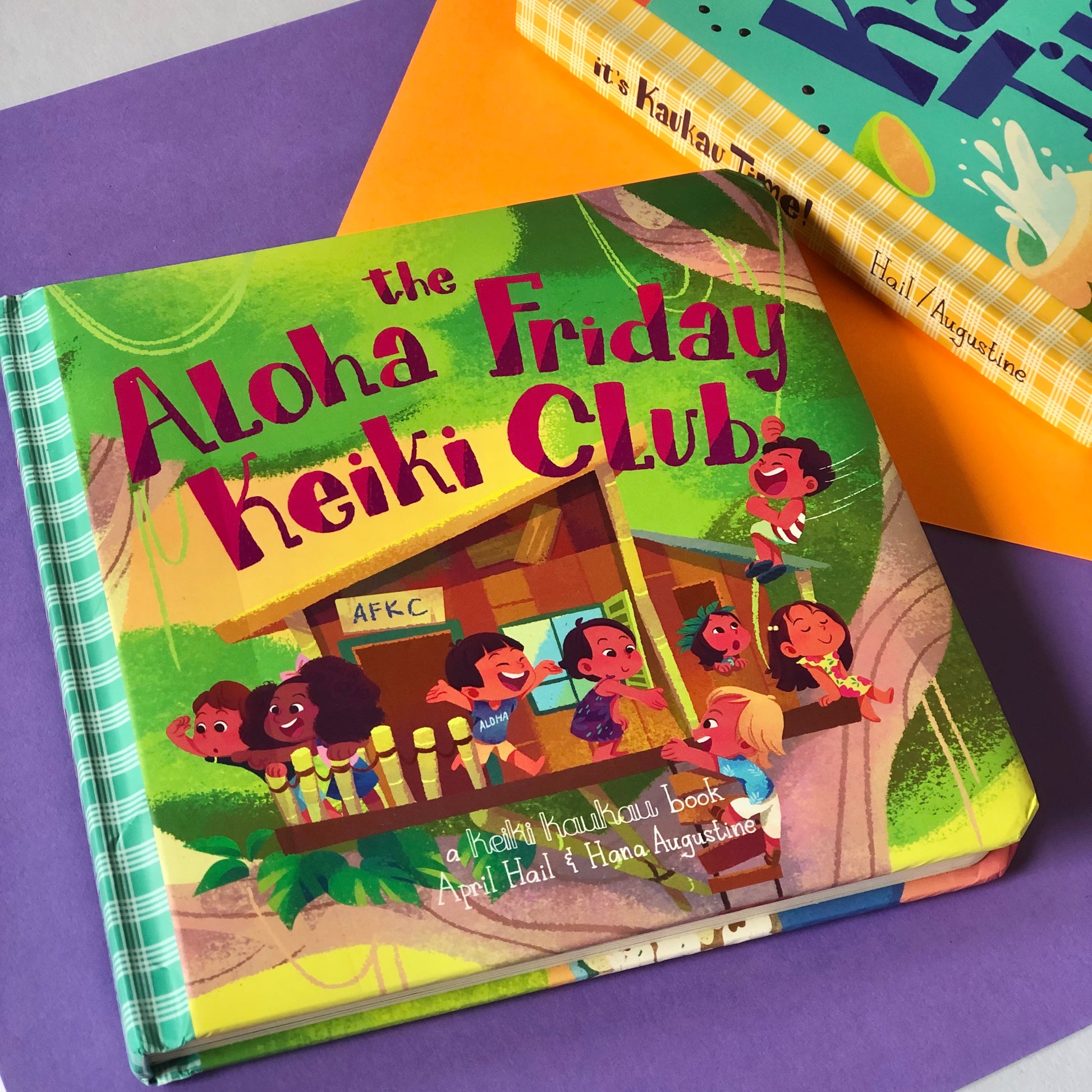 Book with teal palaka print spine and illustration of kids in a tree house reading "The Aloha Friday Keiki Club"