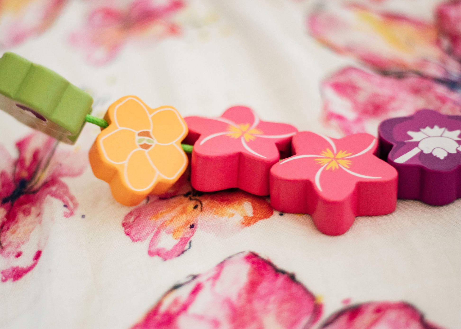 Five wooden flower beads (green orchid, puakenikeni, two pink plumeria, and a purple orchid) strung on a green string