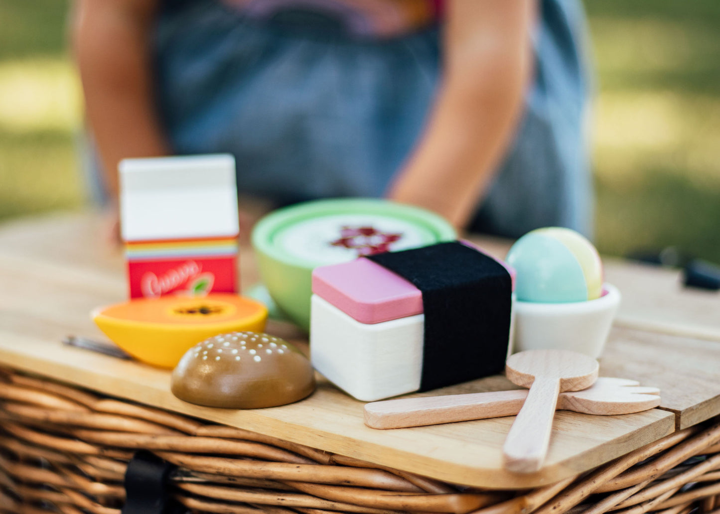 a group of wooden toys (guava juice carton, papaya, poke bowl, malasada, spam musubi, shave ice, fork, and spoon) on a wooden table 