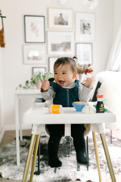 Baby sitting in highchair playing with wooden toys (passion orange juice can, saimin bowl, and shoyu bottle)