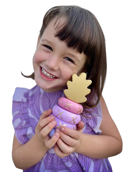 Little girl holding wooden pink, purple, and gold pineapple stacking toy