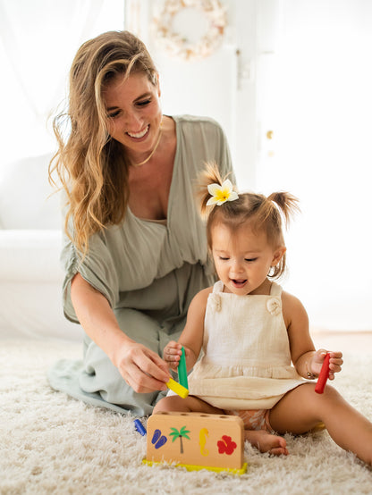 Mother and baby putting pegs into the wooden jumping peg box
